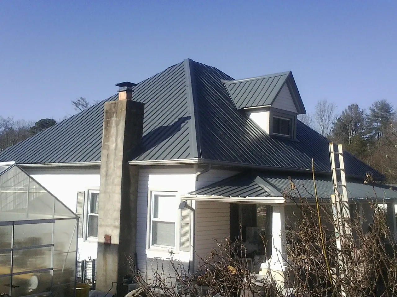 Dark blue standing seam metal roof on a white farmhouse with dormer — Slate & Tile Roof Repair by Roofing Brothers in Newland