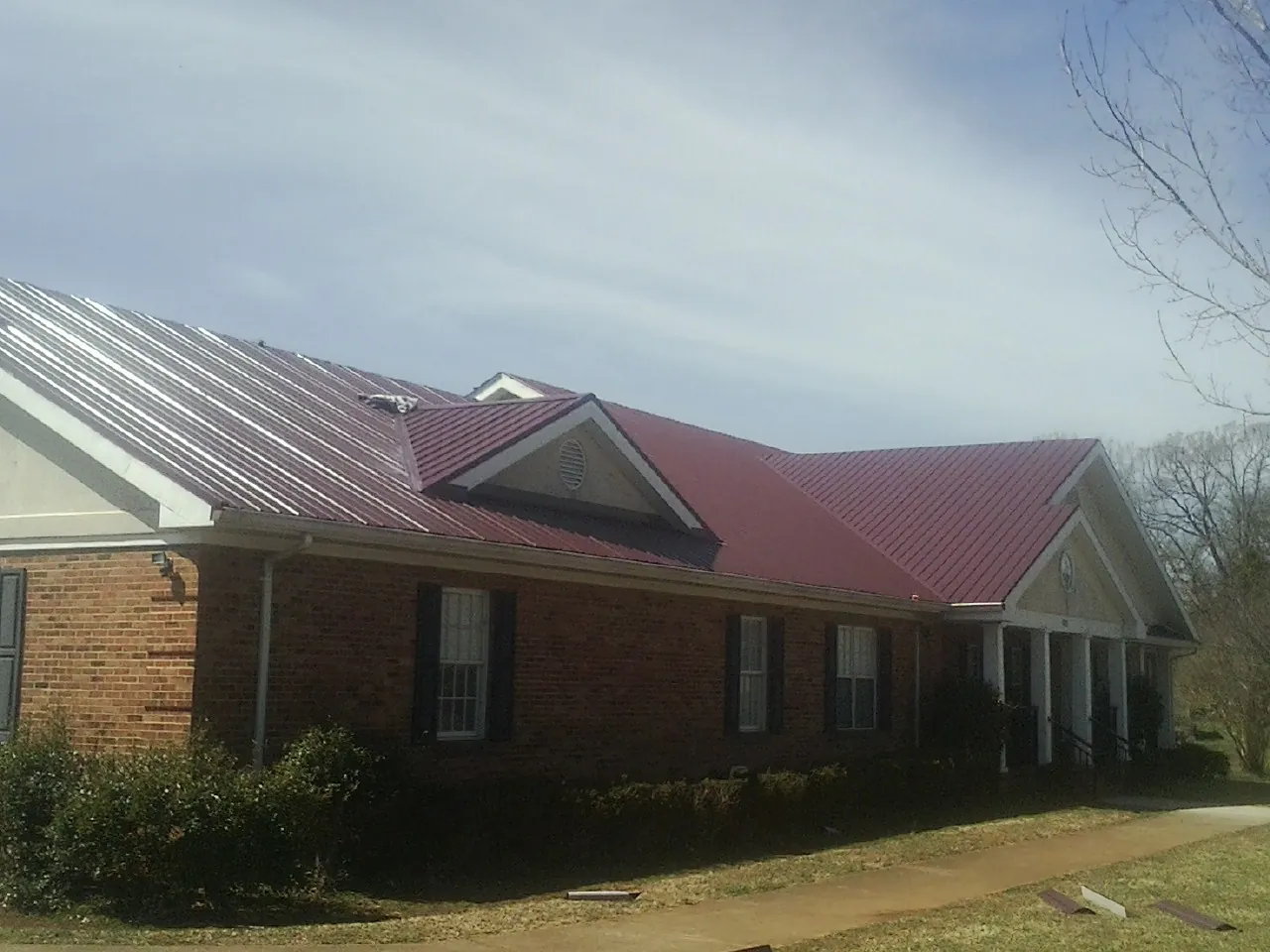 Red metal roof with gabled entries on a long brick building, from a Hail Damage Roof Repair job in Newland