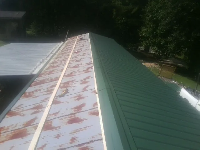 Old rusted panels beside newly installed green metal roofing — Wind Damage Roof Repair by Roofing Brothers in Newland