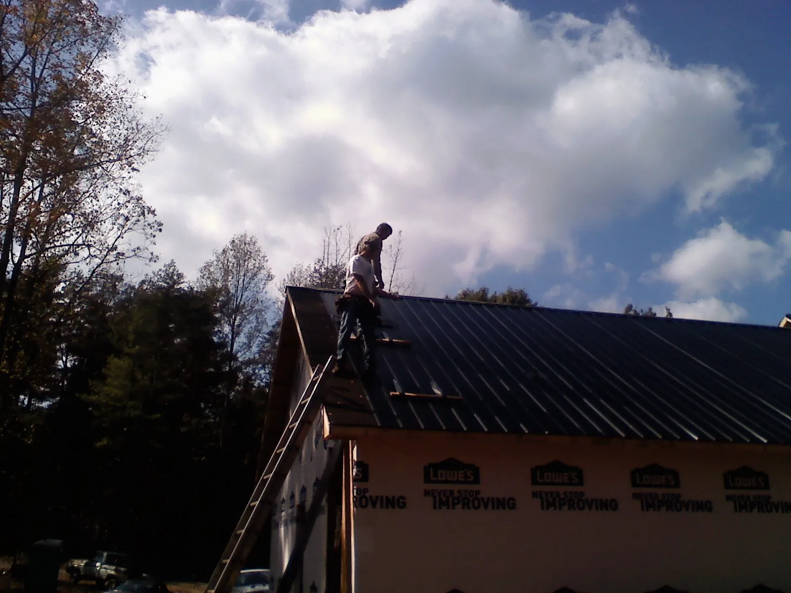 Roofer fastening dark metal panels high against a cloudy sky, from a Roof Inspection job in Newland