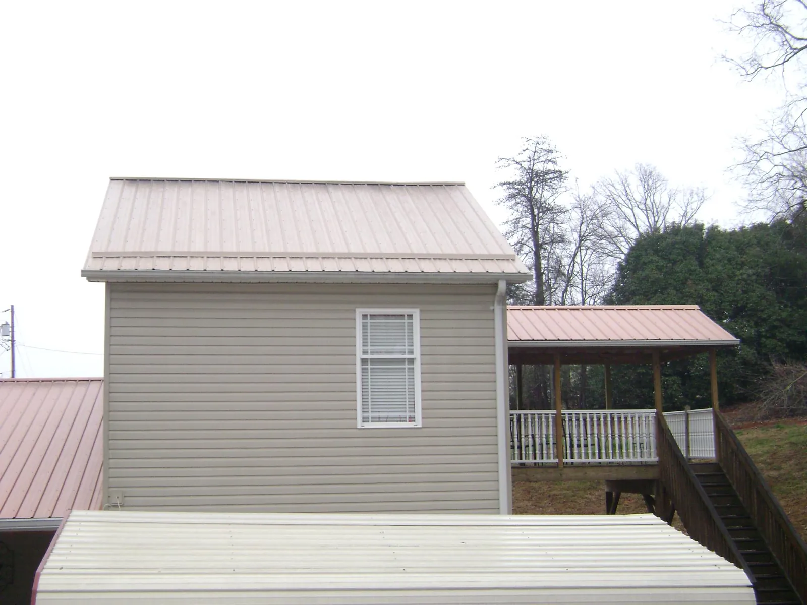 Tan metal roofs on a two story addition and attached porch, from a Roof Replacement job in Newland