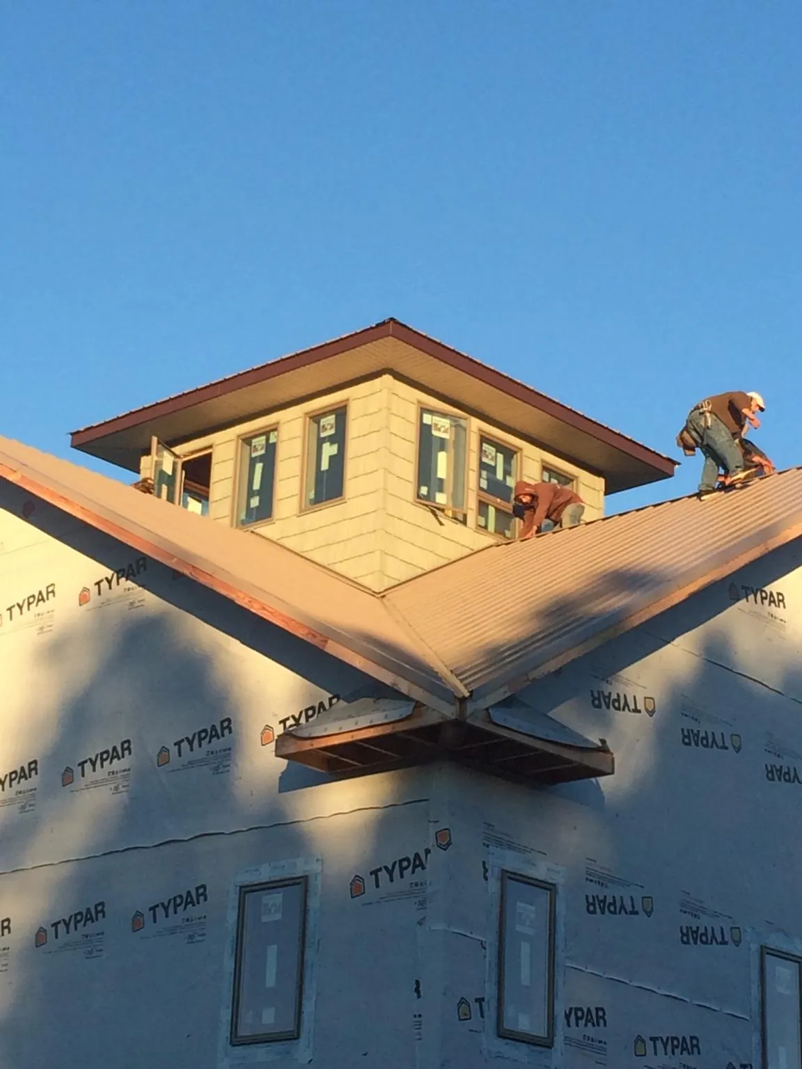 Roofers working around a rooftop cupola on a new metal roof at sunset in Newland